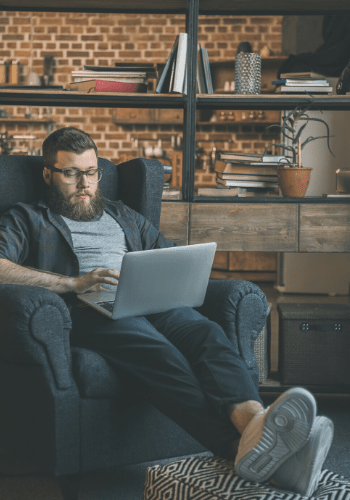Bearded man sitting in an armchair looking at his laptop.