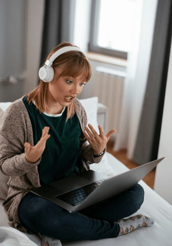 Woman with headphones talking and looking at her laptop.